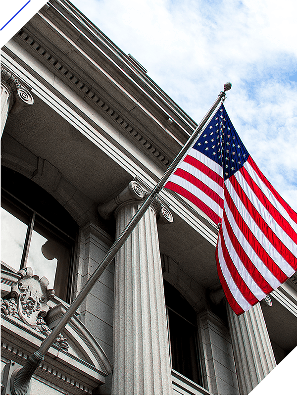 American flag flying over government building in city, blue sky and clouds