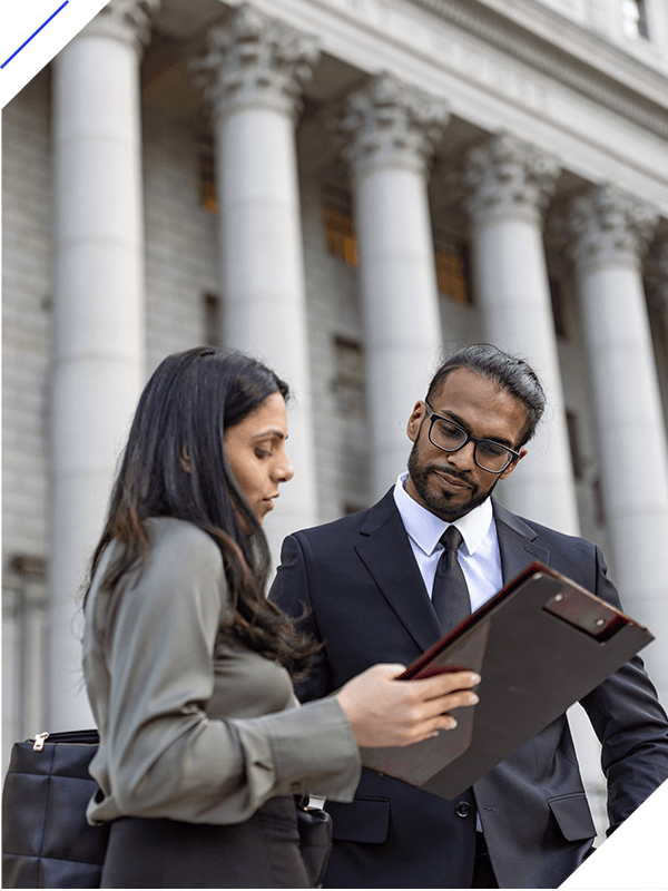 Two professionals, a man and a woman, reviewing documents on a tablet in front of a courthouse.